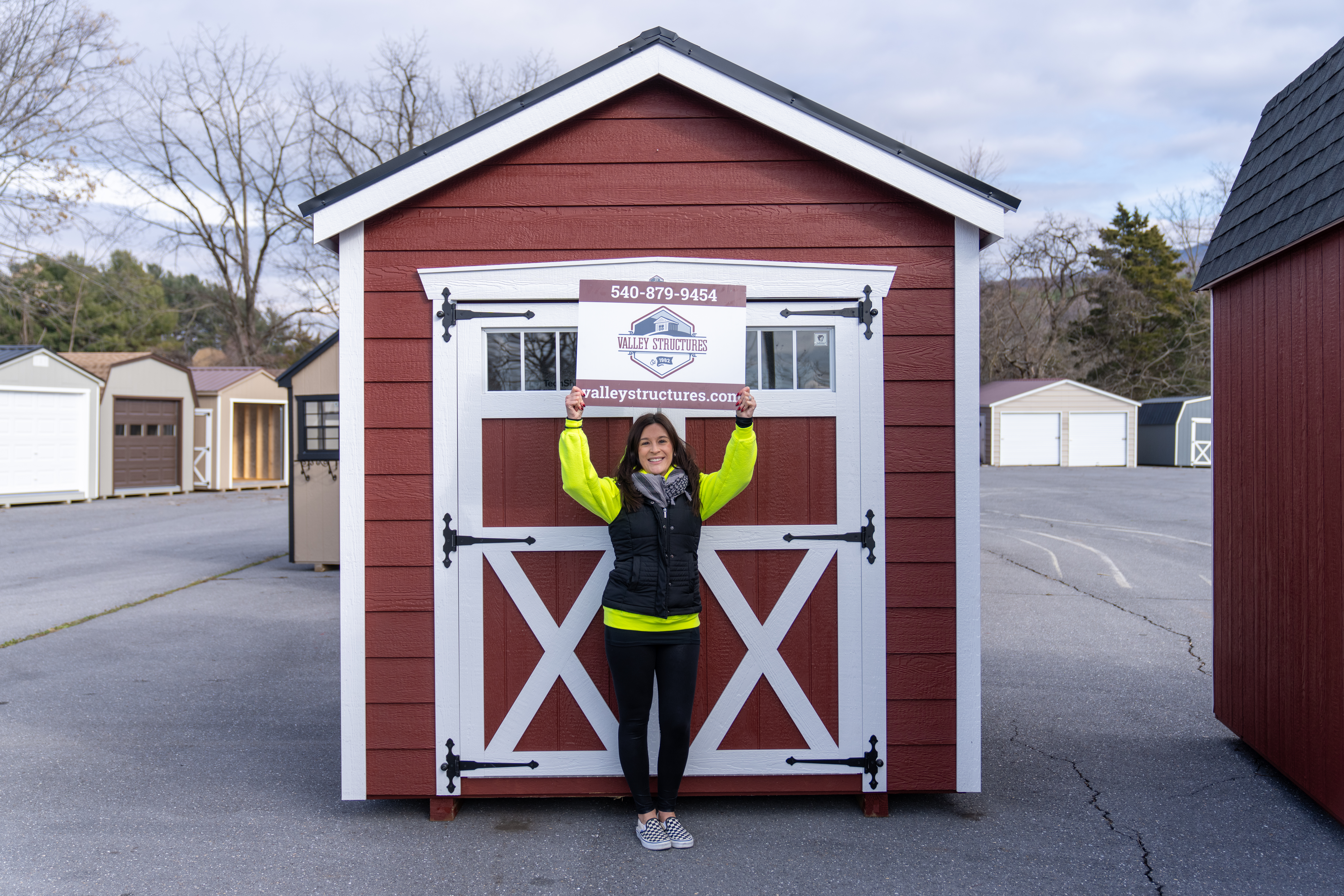 Courtney Hardesty, Estland's Content Marketer, holding a Valley Structures sign above her head in front of red shed that's being given away.