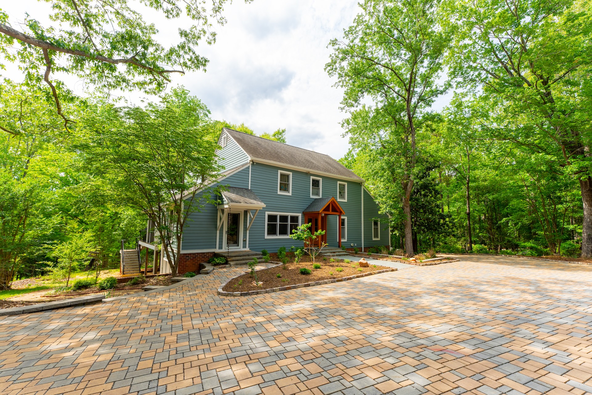 A blue two-story house with a stone driveway and lush green landscaping.