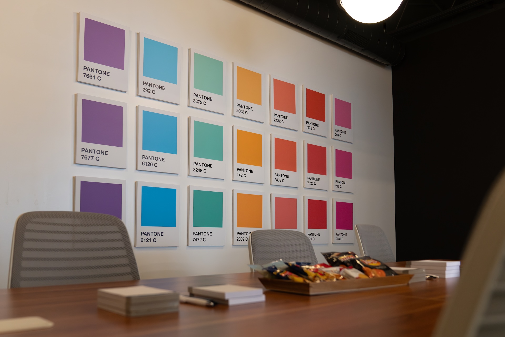 Estland's conference room featuring a long wooden table with snacks in a tray and notepads. On the wall, there is a grid of Pantone color samples in Estland's brand colors, including purple, turquoise, orange and red.