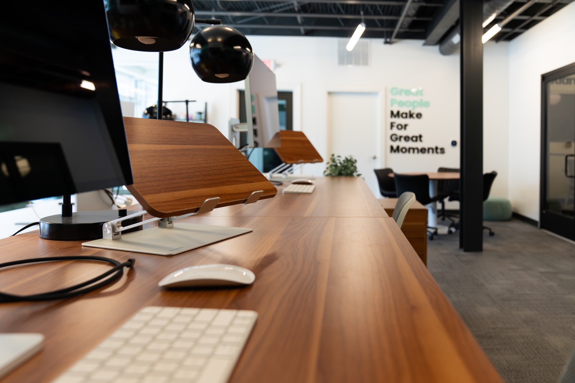 Estland's office interior featuring a long wooden work station with several computer monitors and keyboards. Black pendant lights hang overhead, and there are green plants adding a touch of nature.