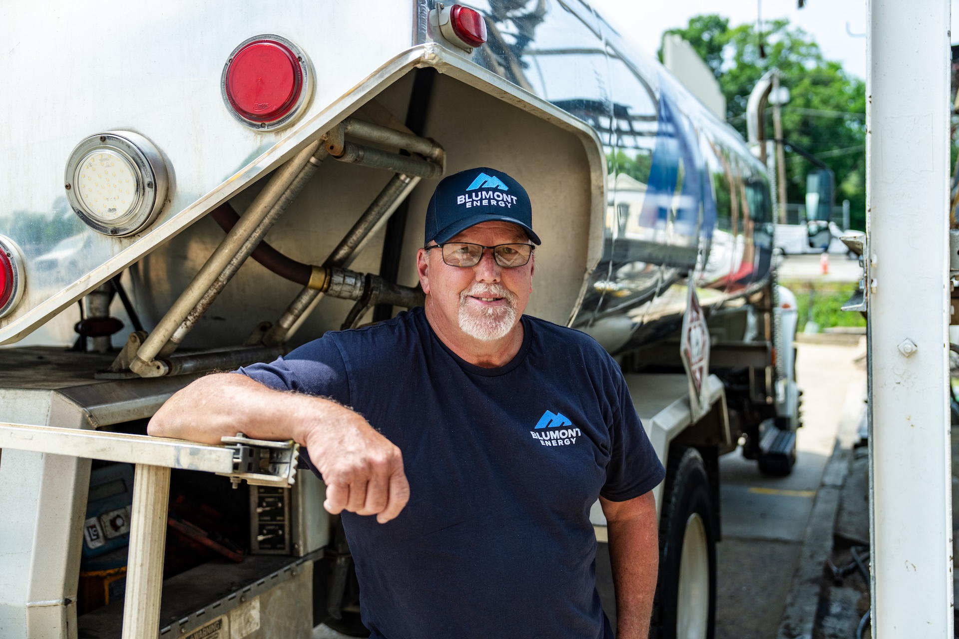 Blumont Energy team member in new custom, branded hat and t-shirt, designed by Estland. He's standing behind a fuel delivery truck.